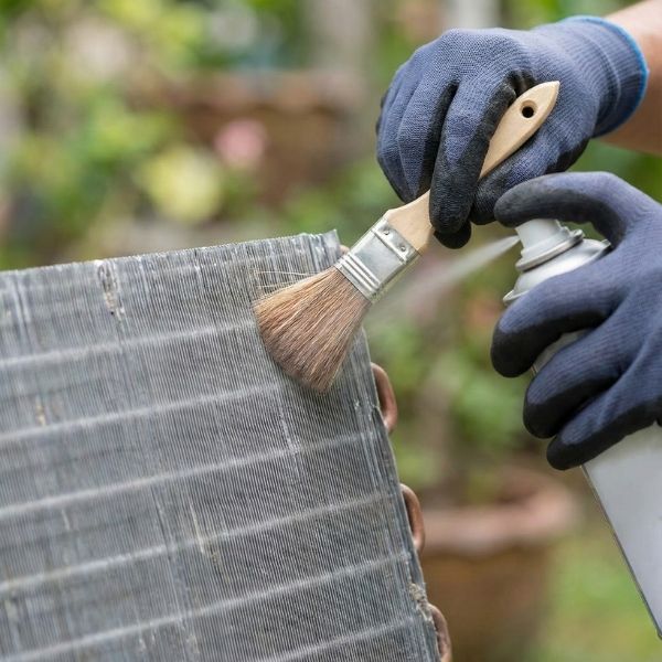A technician carefully cleans the thin metal fins of an air conditioner coil.