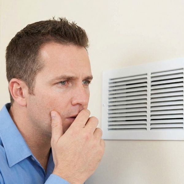A concerned homeowner sniffing the air near an indoor AC vent.